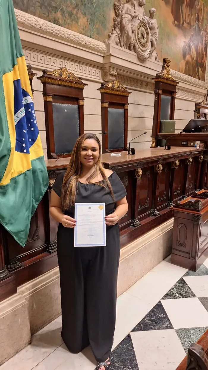 Dra. Nayara Ribeiro no plenário da Câmara Municipal do Rio de Janeiro segurando a moção recebida